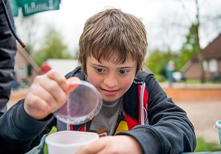 Ein Junge öffnet den Deckel eines unbeschrifteten Plastikbechers um hinein zu schauen.
